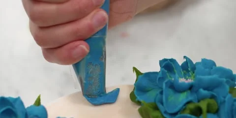 Close-Up of Chef Decorating Cake with Piped Blue Buttercream Flowers Stock Footage 343589343