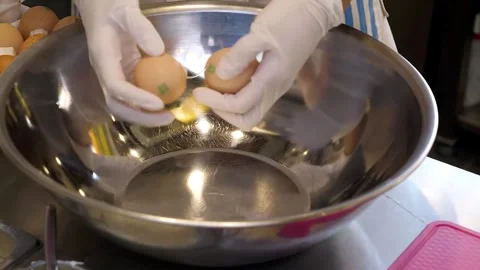 Close-up of a chef in gloves cracking fresh eggs into a large metal bowl. Stock Footage 331772308