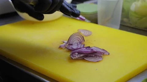 Close-up of a chef in gloves cutting red onions on a chopping board in a kitchen Stock Footage 344038576