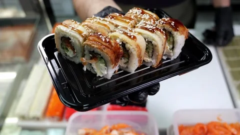 A close-up chef in gloves holds a plate of sushi in the restaurants kitchen. Stock Footage 323910479