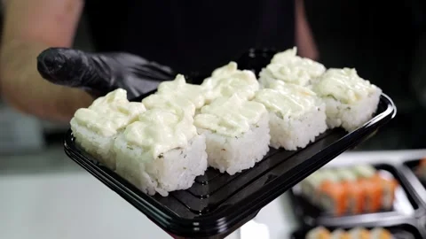 A close-up chef in gloves holds a plate of sushi in the restaurants kitchen. Stock Footage 323911134