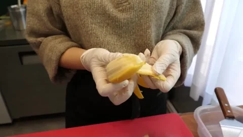 Close-up of Chef in Gloves Peeling a Fresh Yellow Banana over Cutting Board Stock Footage 345692138