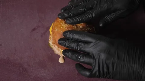 A close-up chef in gloves puts buns with sauce on burgers with tomatoes. Stock Footage 343736486