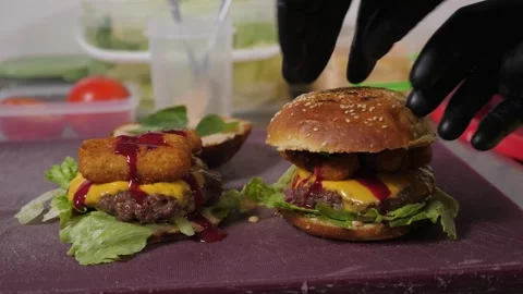 A close-up chef in gloves puts buns with sauce on burgers with tomatoes. Stock Footage 344038616