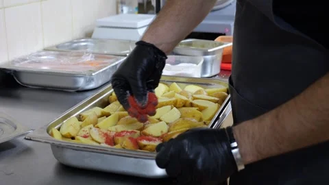 Close-up of a chef in gloves sprinkling raw potatoes with paprika and spices. Stock Footage 320877923