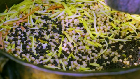 Close-up of chef hand adding raisins to Uzbek plov in large metal cauldron Stock Footage 332974708