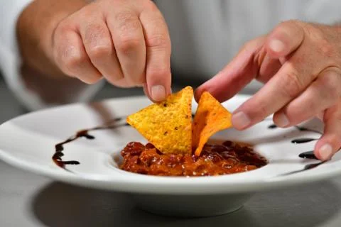 Close up of chef hands adding some nachos to a chili dish on a table Stock Photos