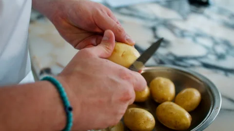 Close up of a chef peeling fresh yellow potatoes with a knife over a metal Stock Footage 337150431