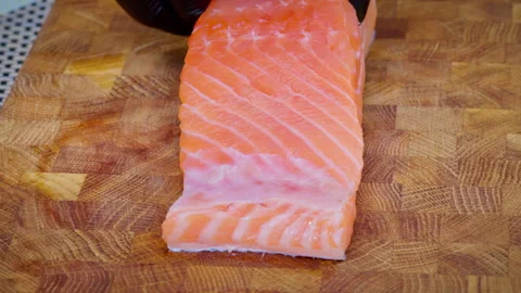 Close-up of a chef placing a raw salmon steak on a wooden cutting board. Video stock 315902701