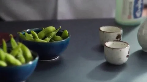Close-up of chef pouring hot sake with bowls of Edamame (soy beans) on the si Stock-Footage 98247443