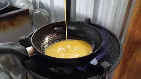 Close-up of Chef Pouring Raw Whisked Eggs into Hot Frying Pan on Gas Stove for O Stock Footage 338211834