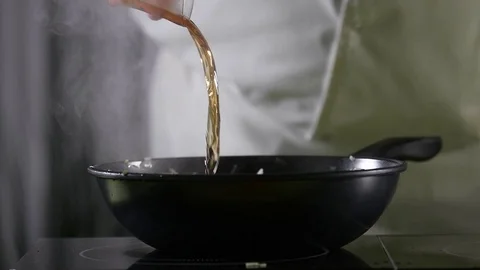 Close-up of a chef pouring a small glass of brandy into a heated bowl in slow Stock Footage 123884793