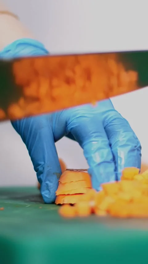 Close-up, the chef, in protective gloves, is cutting carrot on a cutting board. Stock Footage 319939017