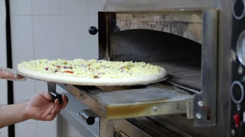 Close-up of a chef putting a large cheese pizza in the oven for baking. Stock Footage 318139578