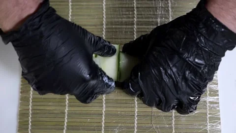 Close-up of a chef putting a sliced cucumber on rolled sushi in the kitchen. Stock Footage 323363223