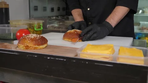 Close-up of the chef of the restaurant in gloves cuts a burger bun with a knife Stock Footage 288334003