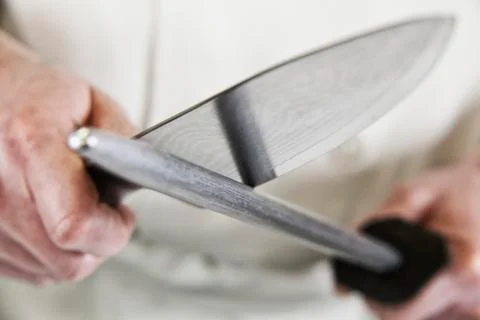 Close-up of a chef sharpening a large kitchen knife blade with a steel. 스톡 사진