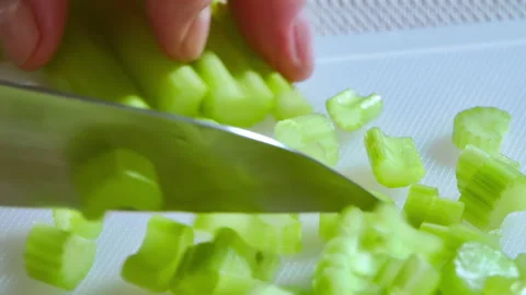 Close-up. A chef is slicing celery stalks on a white kitchen board. Stock Footage 302735316