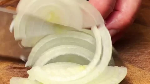 Close up of a chef slicing a fresh white onion with a sharp knife on wooden boar Stock Footage 325032376