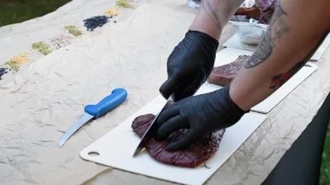 Close-up of Chef Slicing Grilled Steak Outdoors on Rustic Table with Tattooed Stock Footage 339202892