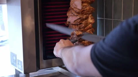 Close-up of a chef slicing shawarma meat with a knife on a spit in a restaurant. Stock Footage 319004344