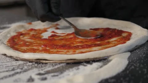 Close-up of the chef spooning tomato sauce onto the pizza dough in the pizzeria. Stock Footage 287583235