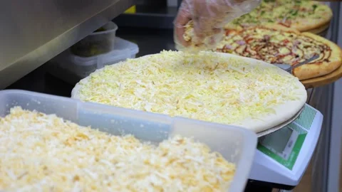 Close-up of a chef sprinkling grated cheese on a pizza in a restaurant kitchen. Stock Footage 318658906