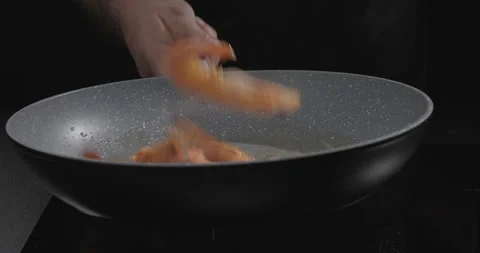 Close-up of a chef tossing shrimp over a frying pan on a black background. The Stock Footage 250243448