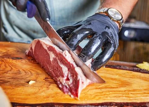 A close-up of a chef using a knife to slice raw steak on a wooden cutting boa Stock Photos