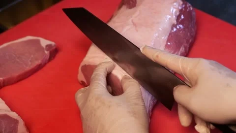 Close-up of chef using a sharp knife to carefully cut pork on a red table Stock Footage 172050115