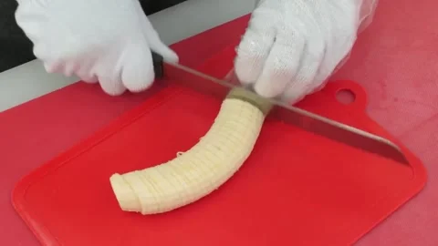 Close-Up of Chef wearing Gloves Slicing a Fresh Banana on a Red Cutting Board 스톡 동영상 345658209
