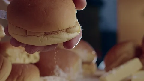 Close-up of chef's hand cutting burger bun in half with sharp knife. 4K slow Stock Footage 111750500
