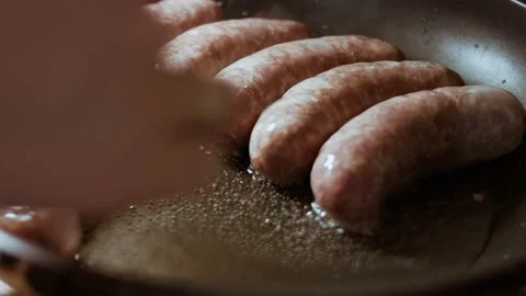 Close-up of chef's hand placing sausages in a black frying pan. Cooking sausages Stock Footage 144321711