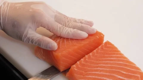 Close-up of Chef's Hand Slicing Fresh Salmon Fillet with Precision Stock Footage 333489445