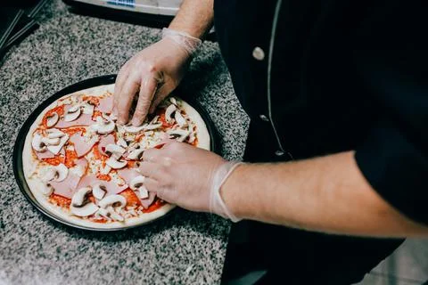 Close-up of the chef's hands adding mushrooms to the pizza toppings Foto stock