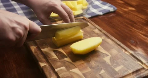 Close up of chefs hands cutting a peeled potato into wedges on a wooden cutting Stock Footage 336189910