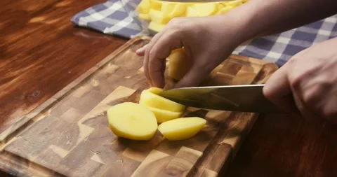Close up of chefs hands cutting a peeled potato into wedges on a wooden cutting Vidéo 336692024