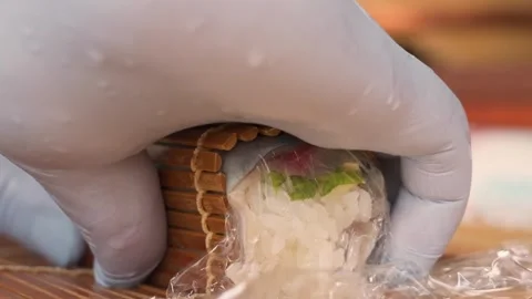 Close-up of Chef's Hands in Gloves Rolling Fresh Sushi with Bamboo Mat Stock Footage 333502034