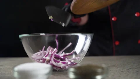 Close-up of a chef's hands pouring sliced onion into a transparent bowl. Salad Stock Footage 152946649