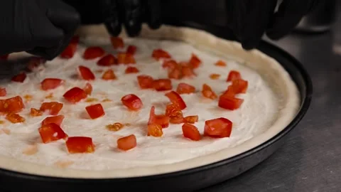 Close up the chef's hands prepare the pizza and put the tomatoes on the dough Stock Footage 261120124