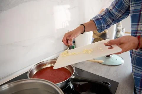 Close-up of chef's hands putting chopped garlic from a cutting board into a.. Stock Photos