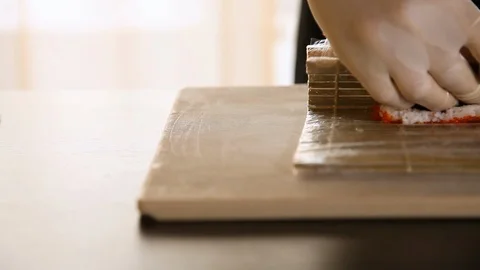 Close-up of chef's hands rolling a sushi roll on bamboo mat.Rice, nori, avocado Stock Footage 119861091