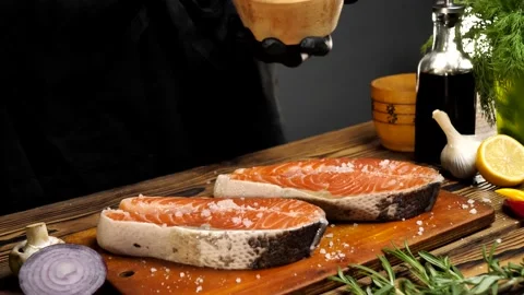 Close-up of Chef's hands salt salmon steaks on a wooden table. Stock Footage 214387627