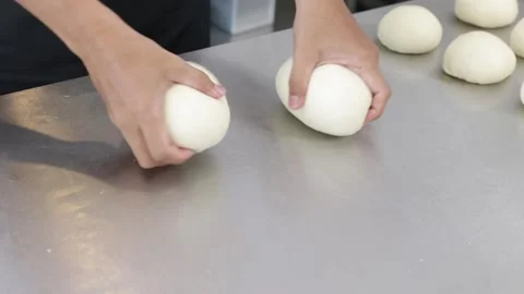 Close-up of a chef's hands shaping soft Japanese bread dough into a round ball Stock Footage 296045750