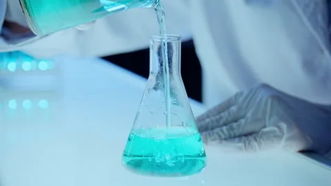 Close Up of Chemist Pouring Blue Liquid from Beaker into Erlenmeyer Flask Stock Footage 337320693