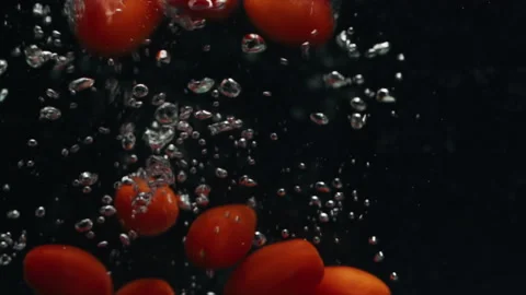 Close-up of cherry tomatoes falling into the water in slow motion. Stock Footage 170788546
