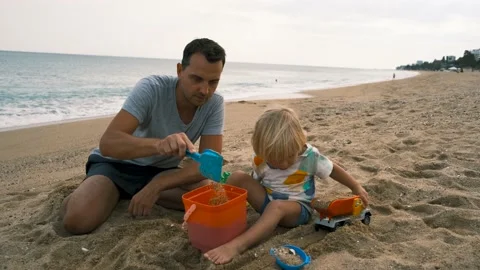 Close-up of a child and his father playing with a shovel and bucket on the sand Stock Footage 220732405