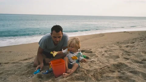 Close-up of a child and his father playing with a shovel and bucket on the sand Stock Footage 220732547