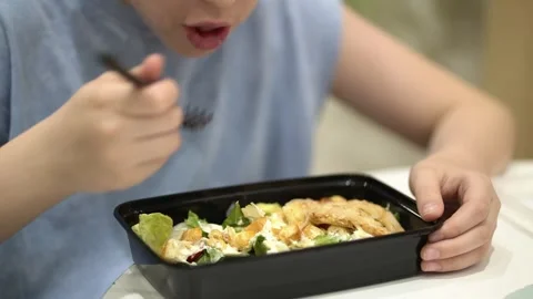 Close-up of a child eating Caesar salad at a shopping mall food court Video stock 343160386