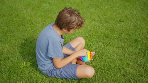 Close-up of a Child Hands Playing with a Popit on Green Nature Background. Kid Stock Footage 155710768
